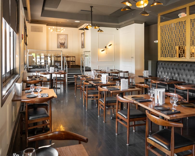 Spacious restaurant dining room with set wooden tables, black chairs, and modern lighting.