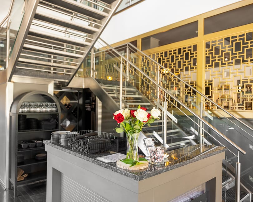 Restaurant reception desk with red and white roses, modern staircase, and gold decorative wall.