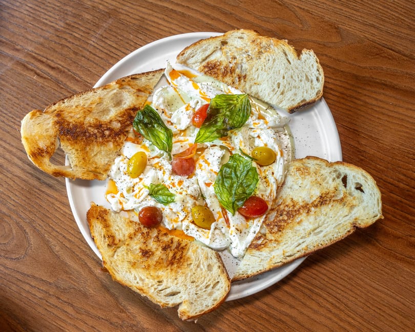 Creamy burrata with colorful cherry tomatoes, fresh basil, and toasted sourdough on a white plate.