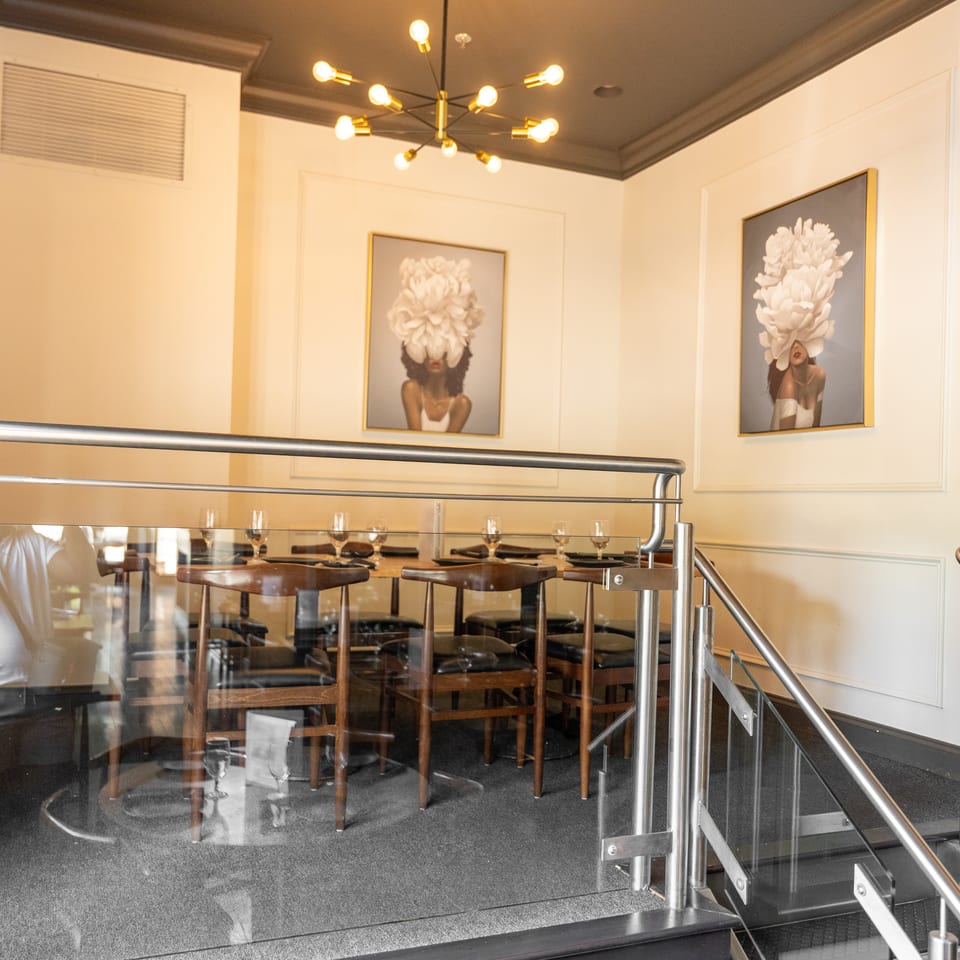 Elegant restaurant interior with set tables behind glass railings and two floral-themed artworks.