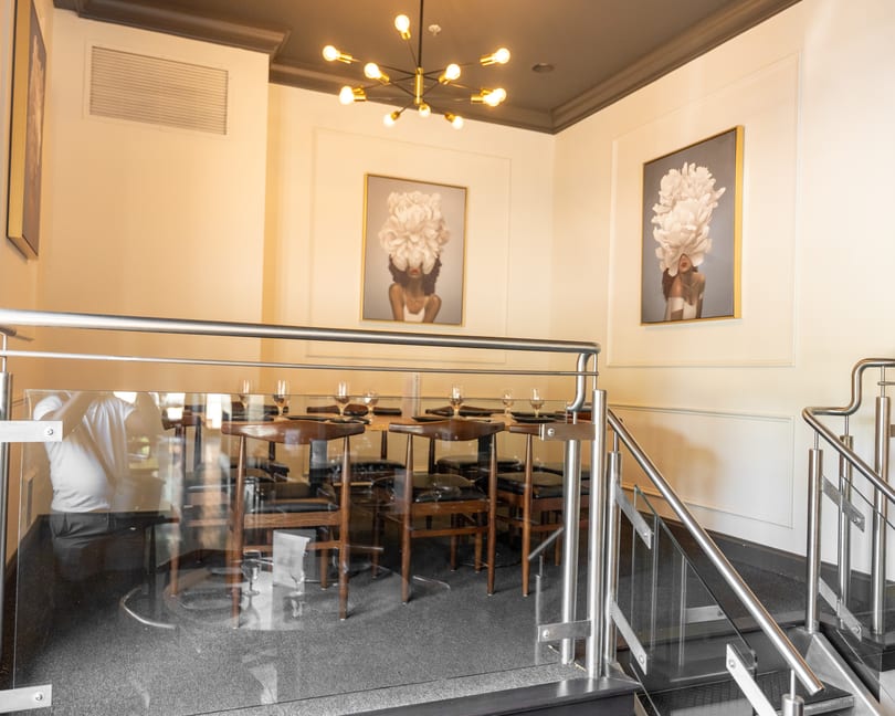 Elegant restaurant interior with set tables behind glass railings and two floral-themed artworks.
