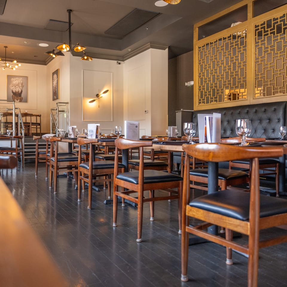 Restaurant dining room with set tables, wooden chairs, dark tufted booths, and golden screens.