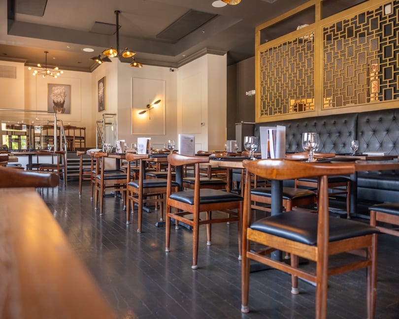 Restaurant dining room with set tables, wooden chairs, dark tufted booths, and golden screens.