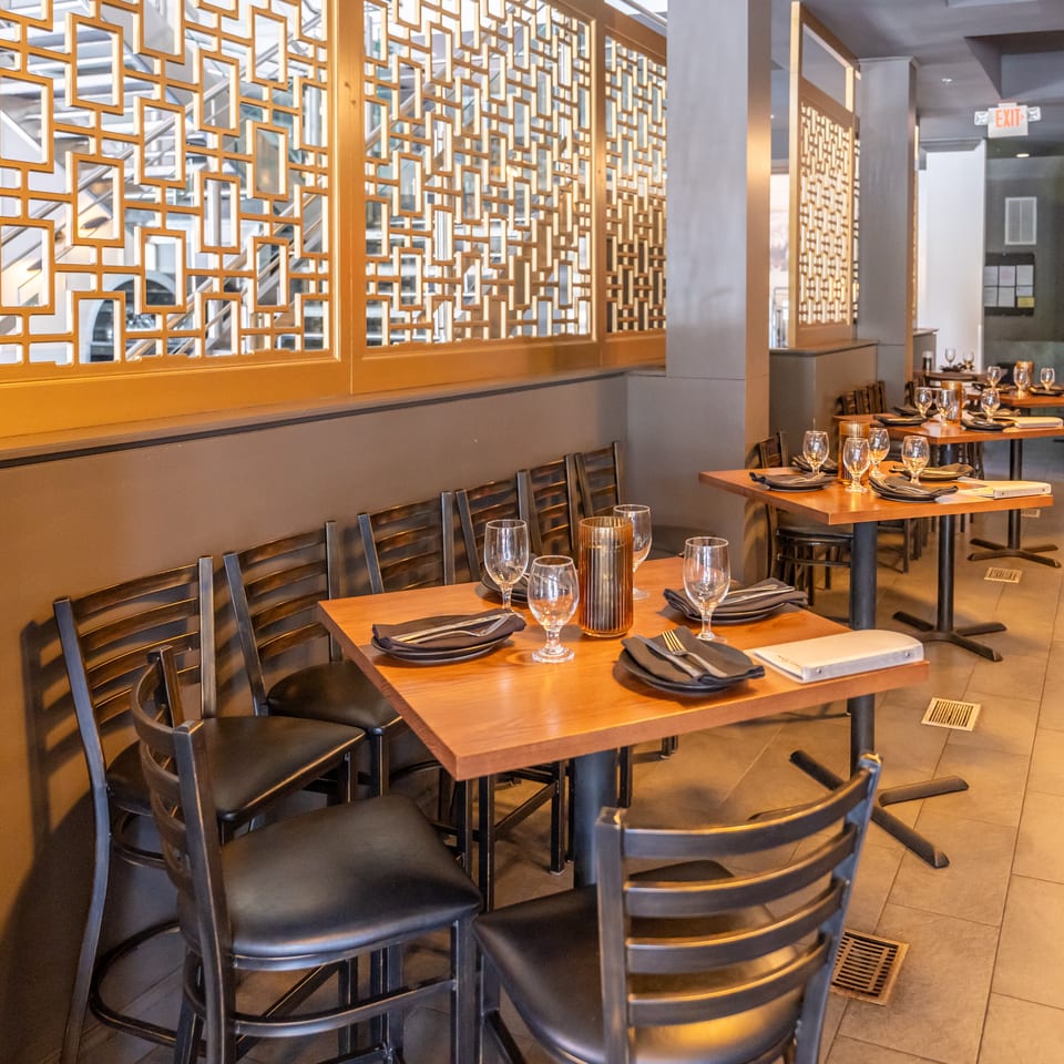 Empty restaurant dining room with set wooden tables, black chairs, and decorative golden wall screens.