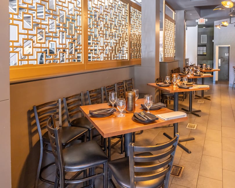 Empty restaurant dining room with set wooden tables, black chairs, and decorative golden wall screens.