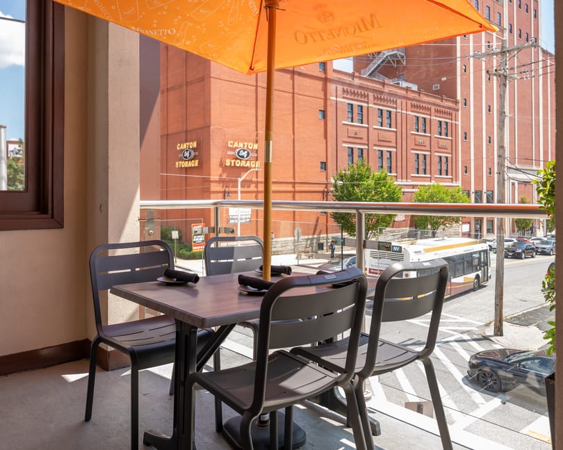 Outdoor patio table and chairs under an orange Mionetto Prosecco umbrella, overlooking a city street.