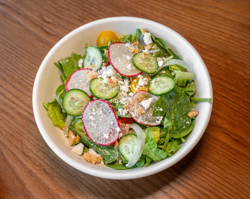 Fresh green salad with sliced radishes, cucumbers, yellow tomatoes, cheese, and croutons.