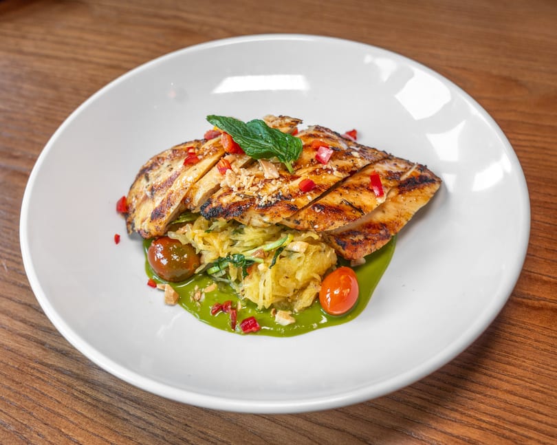 Grilled chicken, spaghetti squash, green sauce, cherry tomatoes, nuts, and mint garnish.