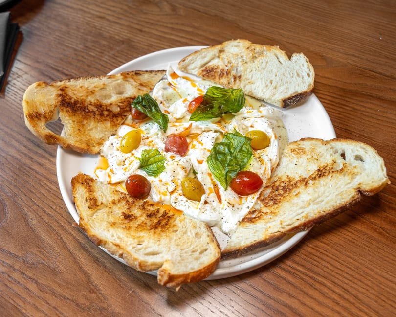 Creamy burrata with colorful cherry tomatoes, fresh basil, and toasted sourdough bread.