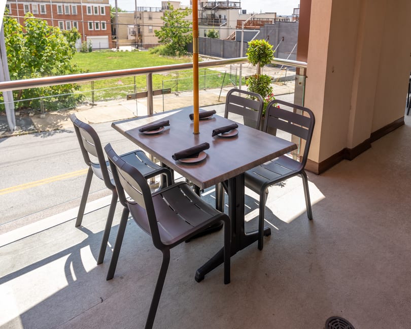 Outdoor restaurant patio with a table set for four, umbrella, and urban street view.