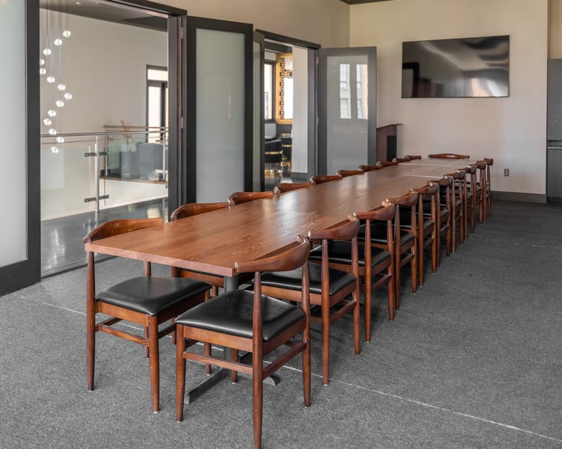 Long wooden conference table with many chairs in a modern meeting room with glass doors and a TV.