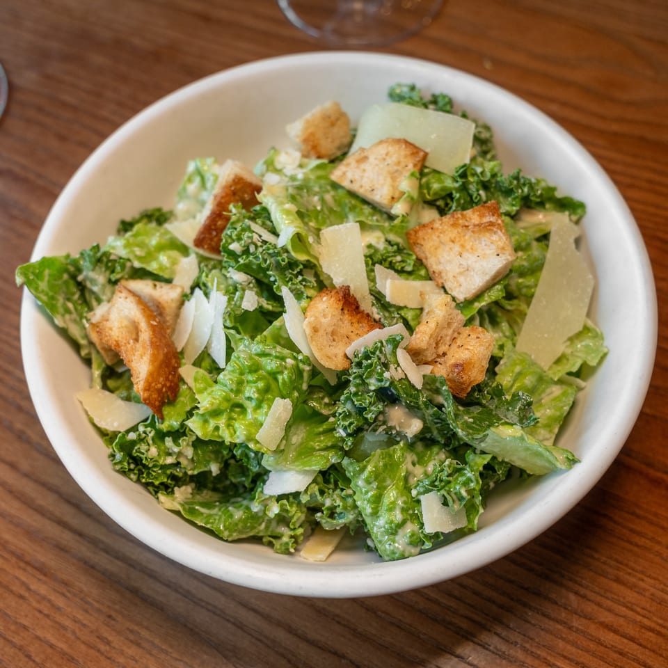 Fresh Caesar salad with romaine, kale, croutons, and parmesan cheese in a white bowl.