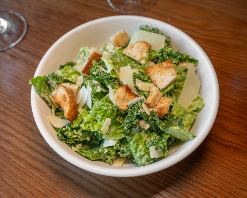 Fresh Caesar salad with romaine, kale, croutons, and parmesan cheese in a white bowl.