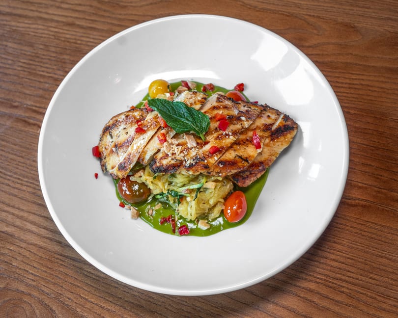 Sliced grilled chicken breast on spaghetti squash with green sauce, cherry tomatoes, and mint.
