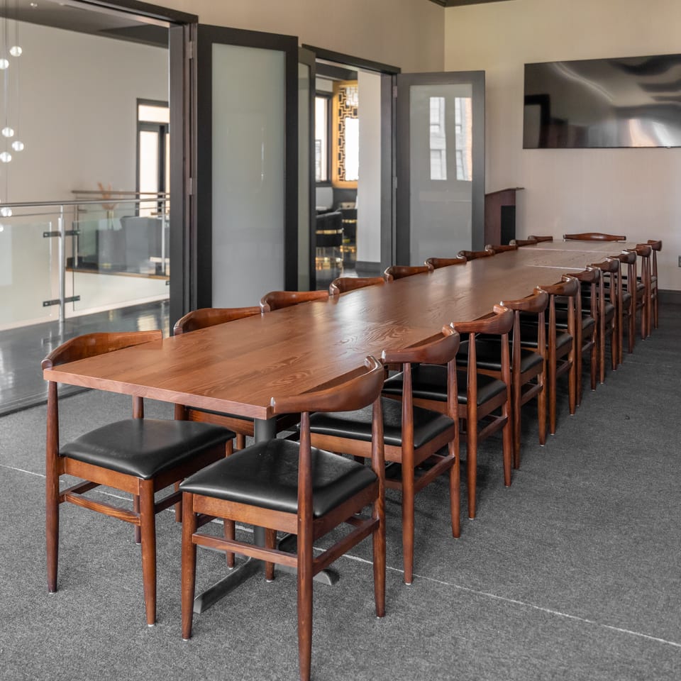 Long wooden conference table with many chairs in a modern meeting room with glass doors and a TV.
