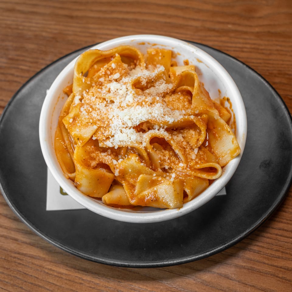 White bowl of pappardelle pasta with tomato sauce and grated Parmesan cheese.