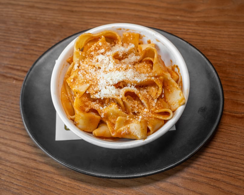 White bowl of pappardelle pasta with tomato sauce and grated Parmesan cheese.