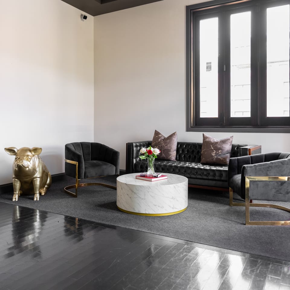 Elegant lounge with a golden pig statue, black sofa, grey chairs, and marble table.