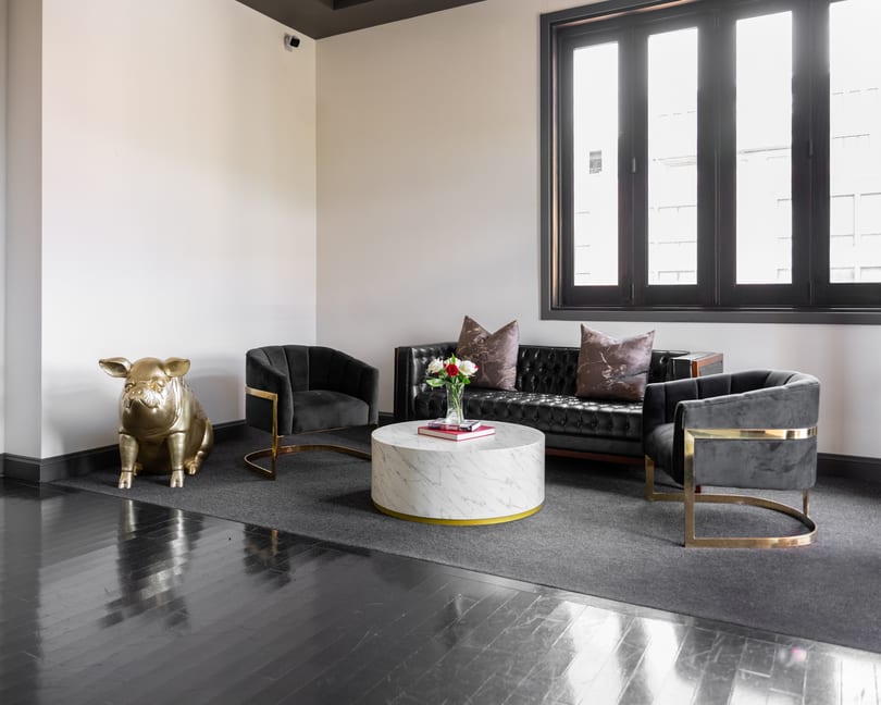 Elegant lounge with a golden pig statue, black sofa, grey chairs, and marble table.
