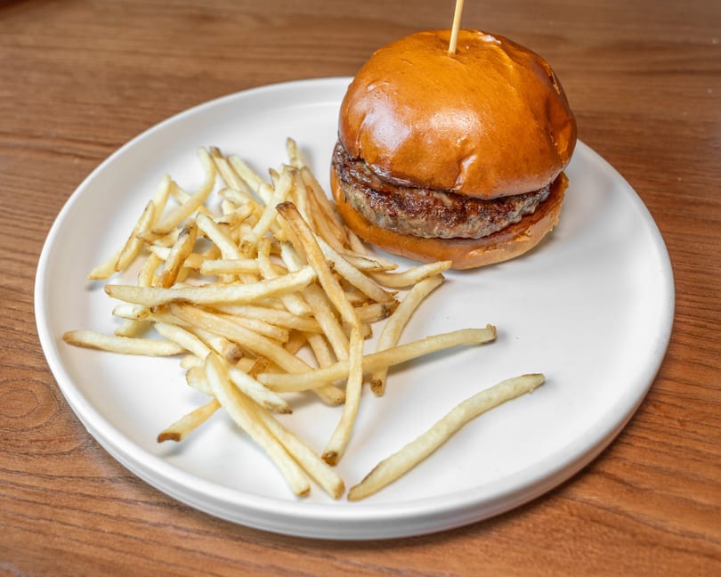 Juicy burger with a golden bun and a side of crispy french fries on a white plate.