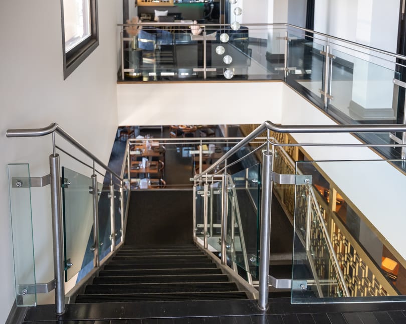 Dark stairs with glass railings lead down to multiple levels of a restaurant dining area.