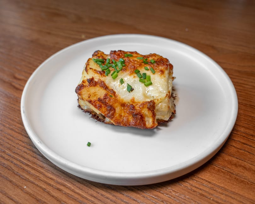 Golden brown potato gratin with melted cheese and chives on a white plate.