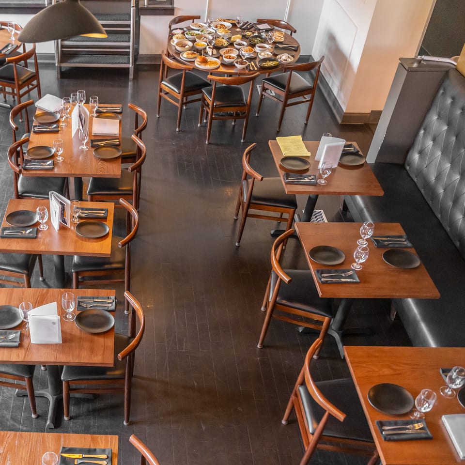 Restaurant dining room with wooden tables, place settings, a large table of food, and a black booth.