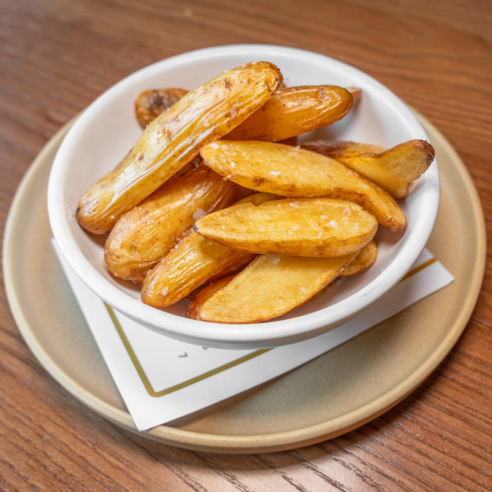 Golden-brown potato wedges sprinkled with salt in a white bowl on a wooden table.